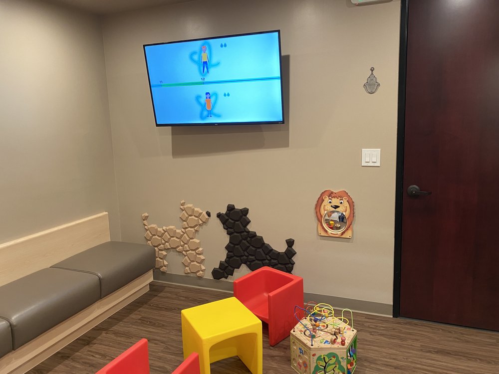 Colorful kids' play area at LA Valley Pediatrics with a lion mirror, animal wall art, and toys